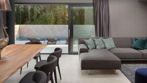 A modern living room with a sofa, dining table, and chairs. There is a glass door leading to an outdoor area with a pool. - Oliva 2 by Interhome (Umag)