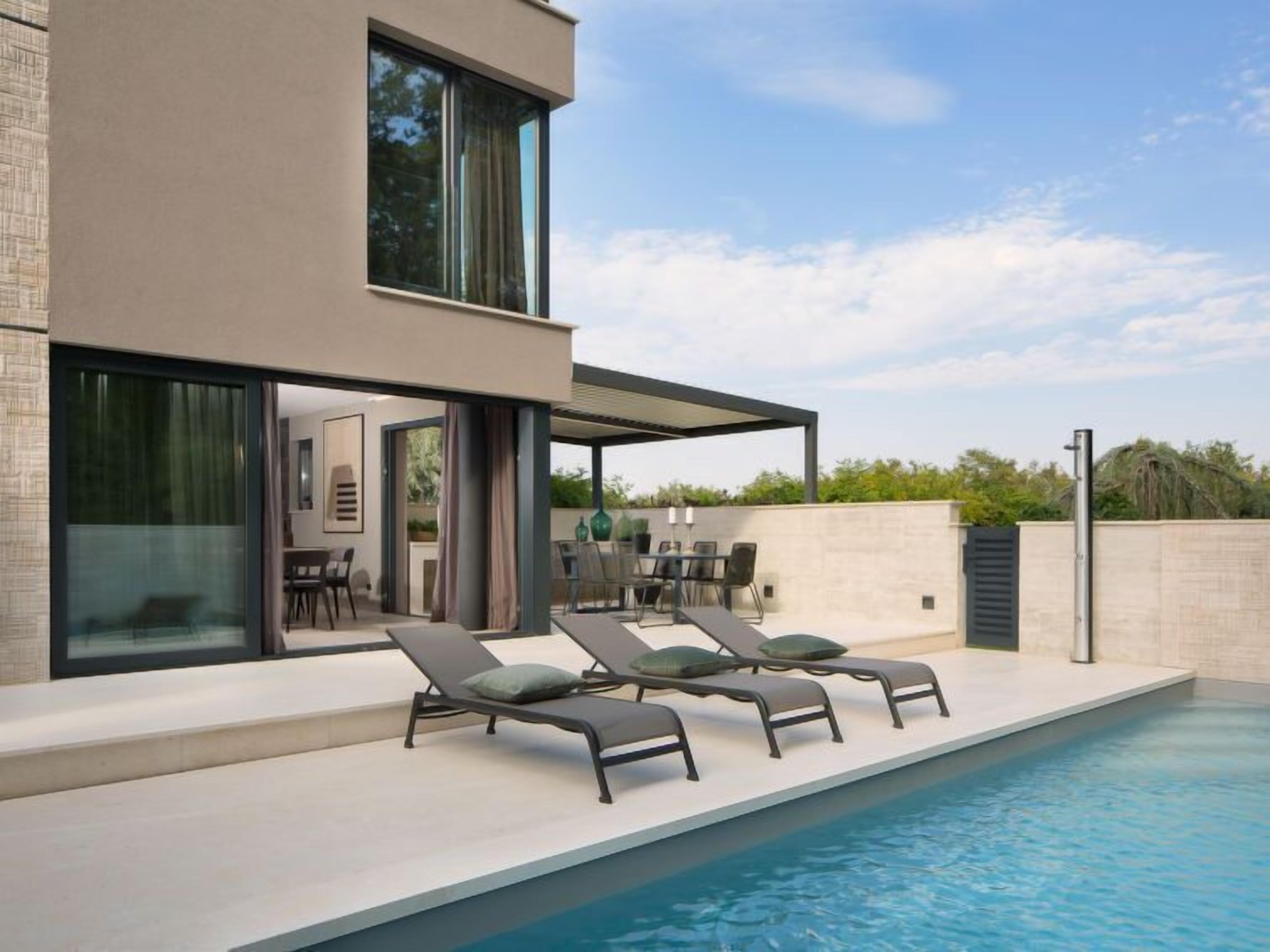 Uma área moderna junto à piscina, com espreguiçadeiras e um espaço coberto para relaxar.