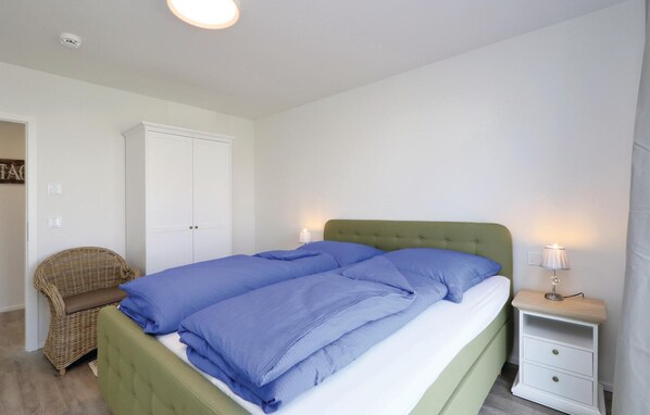 A bedroom with a bed, a nightstand, a wicker chair, and a wardrobe. - Awesome home in OstseeResort Olpenitz with sauna (OstseeResort Olpenitz)