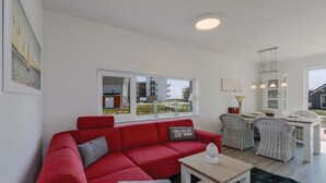 Una sala de estar moderna con un sofá rojo, una mesita y un comedor con sillas de mimbre.