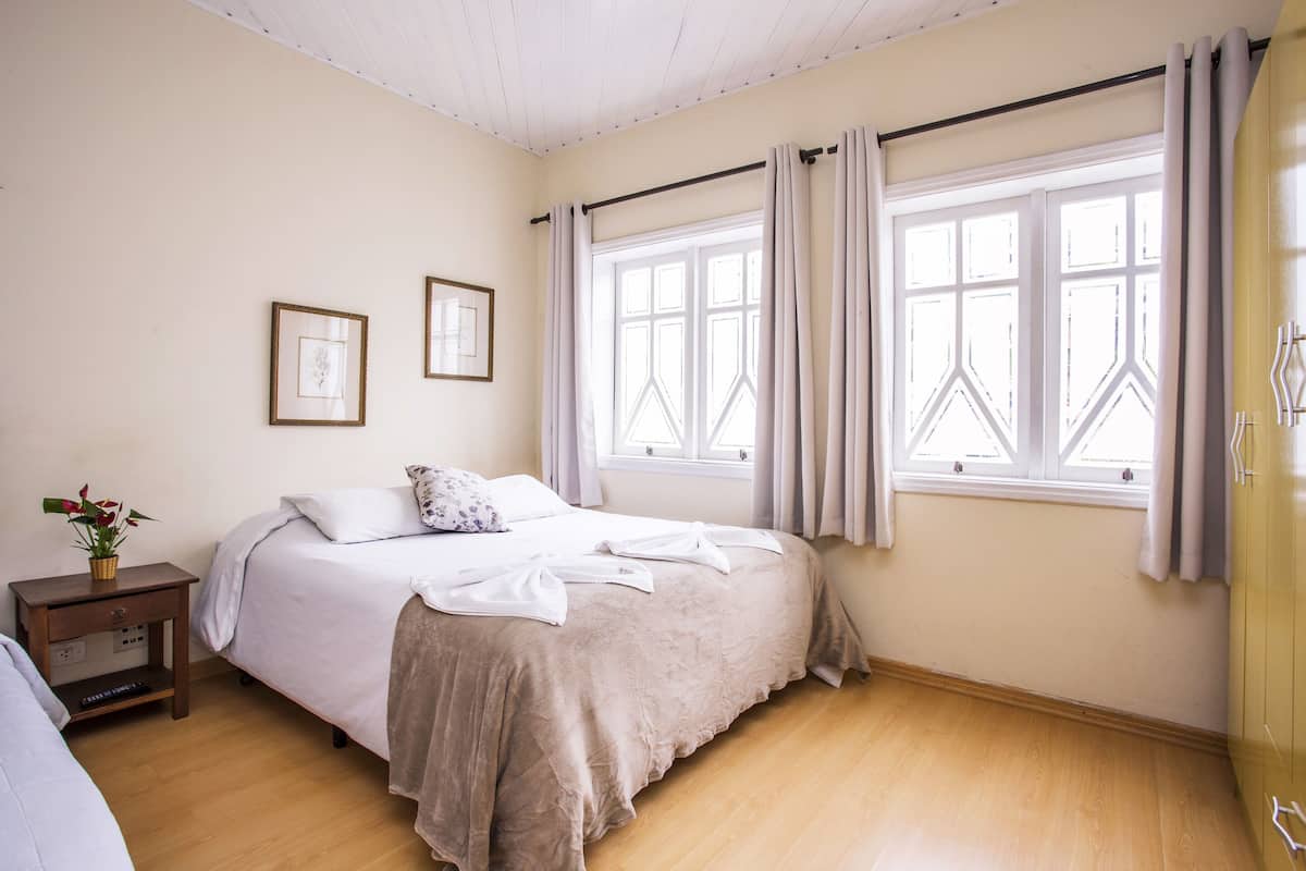 Ein Schlafzimmer mit einem Bett, einem Nachttisch, einem Fenster mit Vorhängen und einem Wandregal.