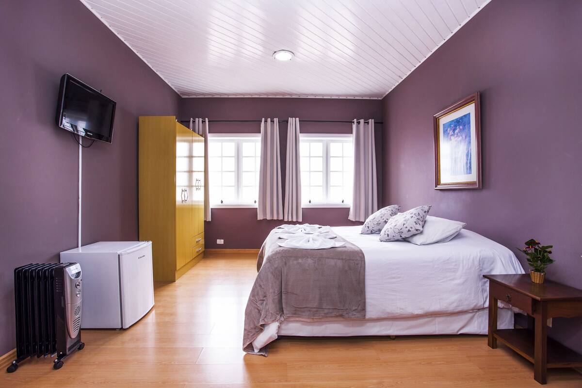 Ein Schlafzimmer mit Bett, Fernseher, Heizkörper und einem Fenster mit Vorhängen.