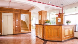 Un comptoir d’accueil en bois, agrémenté d’une plante en pot, un escalier et une porte avec une pancarte.