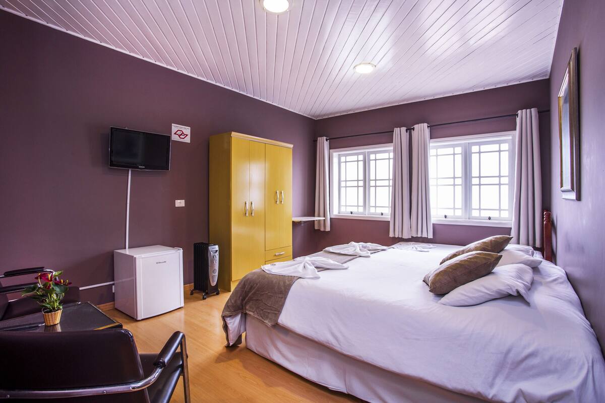 Ein Hotelzimmer mit Bett, Schreibtisch, Kleiderschrank, Fernseher und einem Fenster mit Vorhängen.