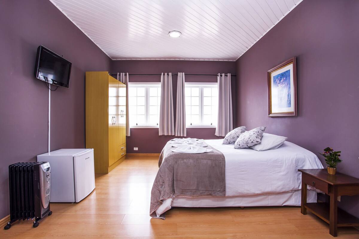Ein Schlafzimmer mit einem Bett, einem Fernseher, einem Heizkörper und einem Fenster mit Vorhängen.