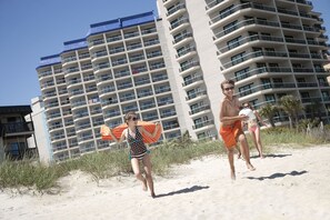 Ein Strandhotel mit mehreren Balkonen und einem Sandstrand im Vordergrund.