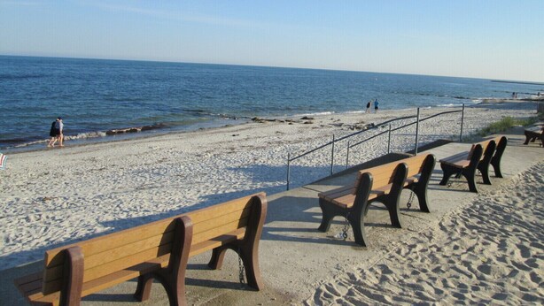 Ein Strand mit Holzbanken und einem Betonweg.