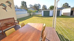 Een houten terras met een tafel, stoelen, een houten bank en een overdekte patio.