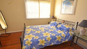 Een slaapkamer met een bed, een lamp, een stoel en een raam met jaloezieën.
