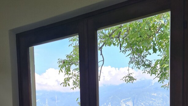 Ein Zimmer mit einer großen Glasschiebetür, die auf einen Balkon mit Blick auf eine gebirgige Landschaft führt.