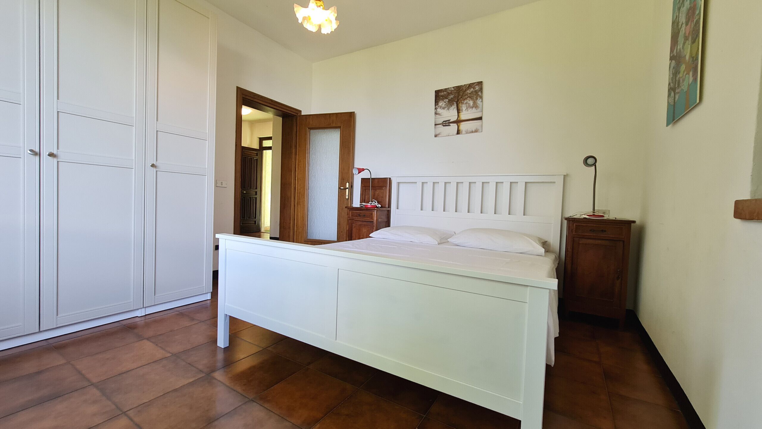 Ein Schlafzimmer mit einem Bett, einem Kleiderschrank, einem Nachttisch und einer Tür zu einem anderen Raum.