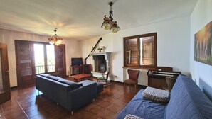 Ein Wohnzimmer mit Sofa, Fernseher, Kamin, Klavier und einem großen Fenster.