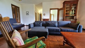 Ein Wohnzimmer mit einem dunkelblauen Ecksofa, einem Holzschaukelstuhl mit kariertem Kissen und einem Holztisch.
