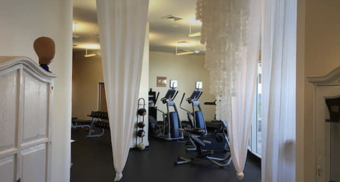 A gym with exercise equipment, including treadmills and stationary bikes, and a staircase with a white balustrade.