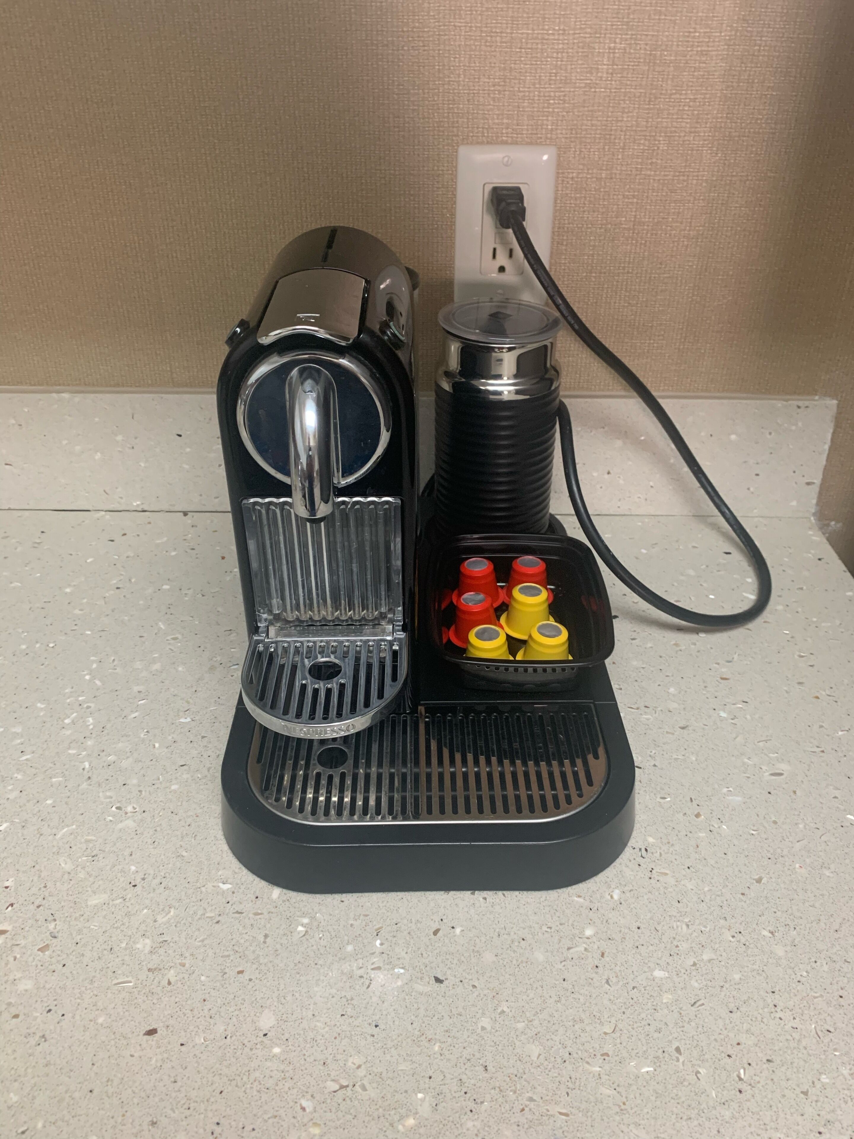 A coffee machine with a water reservoir and a power cord plugged into a wall socket.