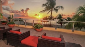 A balcony with wicker furniture and potted plants, overlooking a sunset over the ocean. - ★★★★★ Hotel 1 Bedroom Suite with ocean view ! Lic :STR-01360 Minimum 3 months.  (Sunny Isles Beach)