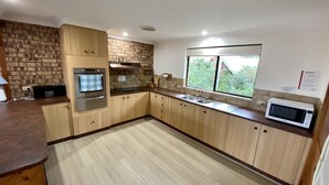 A modern kitchen with wooden cabinets, a built-in oven, a microwave, and a large window offering a view of greenery.