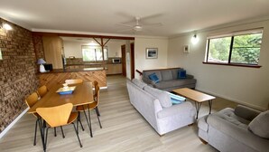 A modern living room with a dining area, grey sofas, a wooden dining table, and a kitchen in the background.
