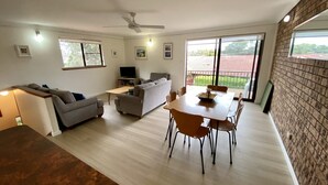 A spacious living area with a sofa, a dining table with chairs, a television, and a balcony with a view.