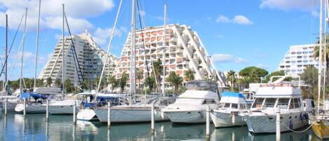 A marina with multiple yachts docked, surrounded by modern high-rise buildings with balconies.