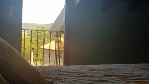 Ein Zimmer mit Bett, Fenster und Blick auf einen Balkon mit Geländer.