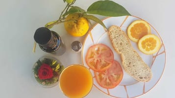 A plate with sliced tomatoes, orange slices, and bread, a glass of orange juice, a lemon, and a small decorative item with a red rose.