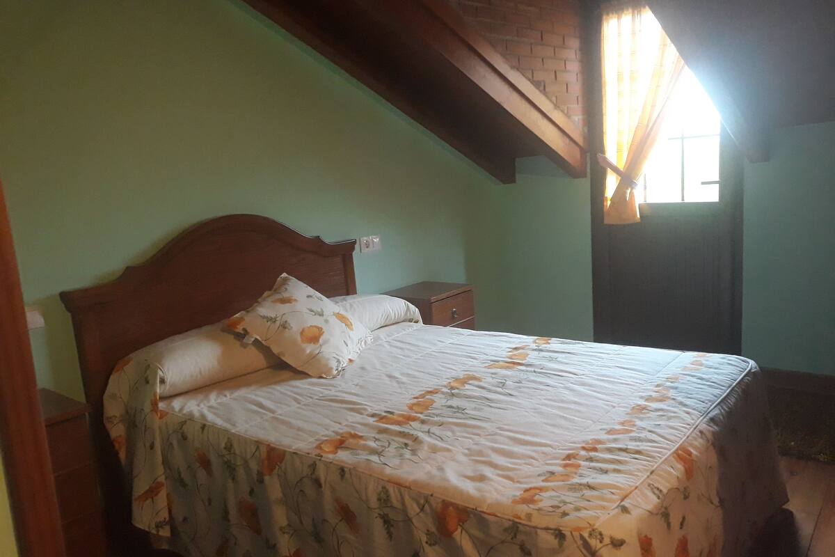 Un dormitorio con estructura de cama de madera, colcha estampada con motivos florales y una mesita de noche.