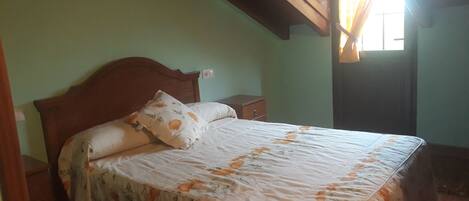 Quarto com estrutura de cama de madeira, colcha florida e mesa de cabeceira.