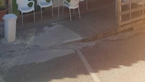 Ein zweistöckiges Gebäude mit grüner Fassade, einer roten Markise und einem Schild mit der Aufschrift "POSADA BAR KABANA". Draußen stehen Tische und Stühle bereit, und ein blauer Sonnenschirm spendet Schatten.