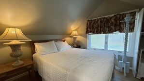 Ein Schlafzimmer mit einem großen Bett, zwei Nachttischlampen, einem Fenster mit Vorhängen und einem Holzboden.