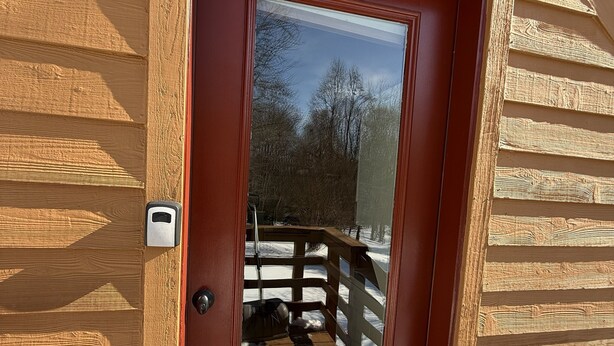 Eine Holzhütte mit roter Tür, einem Glasfenster und einer Holzterrasse.