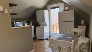 Eine kompakte Küche mit Mikrowelle, Toaster und Kühlschrank. Ein Esstisch mit Stühlen steht unter einer geneigten Decke.