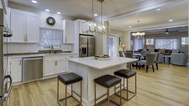 A modern kitchen with white cabinetry, a central island with stools, stainless steel appliances, and recessed lighting. - 109 South Forest Beach - Steps away from your toes in the sand! (Hilton Head Island)