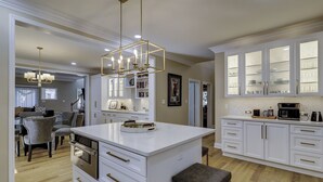 A modern kitchen with white cabinetry, a central island, and a hanging light fixture. - 109 South Forest Beach - Steps away from your toes in the sand! (Hilton Head Island)