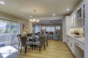 A spacious dining area with a round table and chairs, a kitchen with white cabinets and gold handles, and a balcony with a railing.