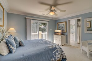 Een slaapkamer met een bed, een plafondventilator, een dressoir, een stoel en een deur naar een andere kamer.