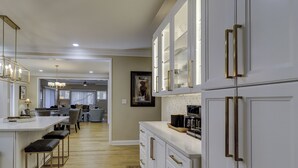 A modern kitchen with white cabinetry and gold handles, a bar area with stools, and a dining area in the background. - 109 South Forest Beach - Steps away from your toes in the sand! (Hilton Head Island)