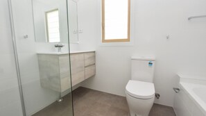 Baño con inodoro, lavamanos y cabina de ducha de vidrio.