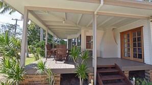 A covered outdoor area with a wooden deck, a brick wall, and a wooden staircase leading to a door. - Tranquil Waters - 30 Camden Head Rd Dunbogan (Dunbogan)