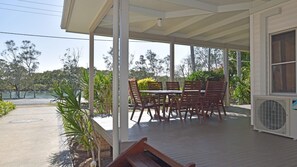 Un patio al aire libre cubierto con una mesa y sillas, rodeado de plantas y vistas a un cuerpo de agua.