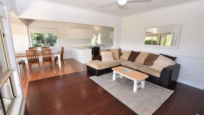 A modern living room with a sectional sofa, a dining area with wooden chairs, and a kitchen in the background. - Tranquil Waters - 30 Camden Head Rd Dunbogan (Dunbogan)
