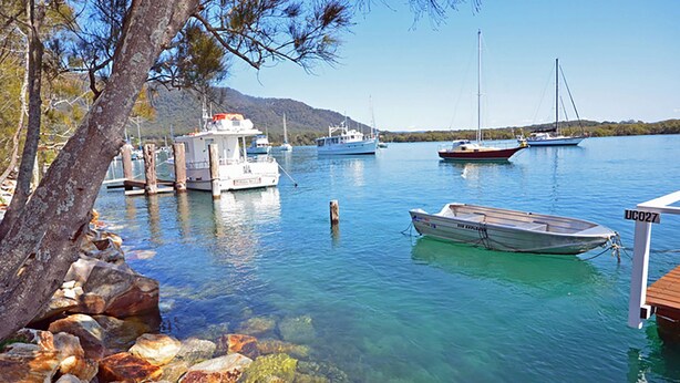 A marina with boats docked, clear water, and a rocky shoreline with trees. - Tranquil Waters - 30 Camden Head Rd Dunbogan (Dunbogan)