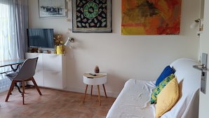A living room with a TV, a desk, a chair, a small side table, and a bed with pillows. - Studio 2 Pers. Pines View in Building Facing sea Baie de La Baule (La Baule-Escoublac)
