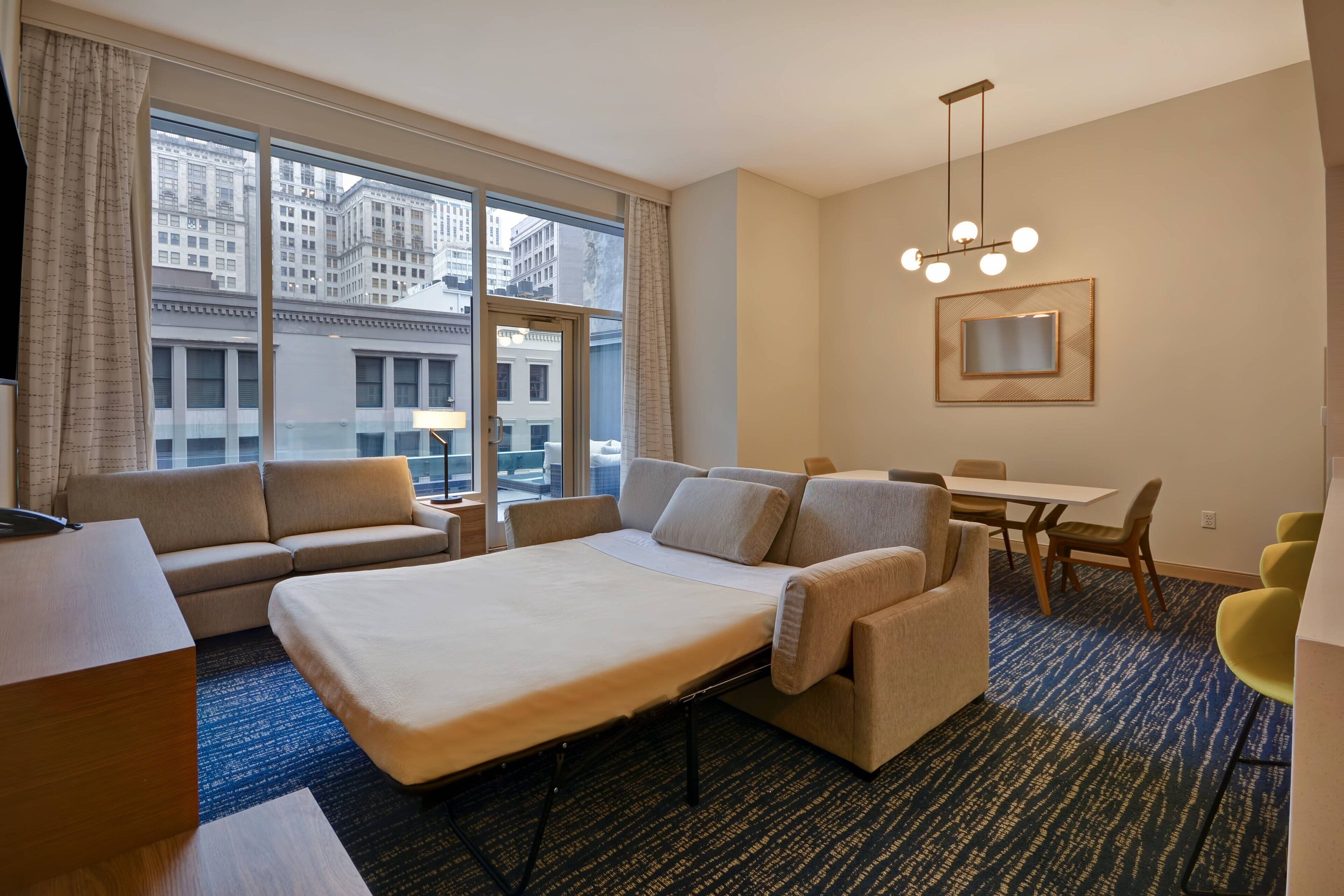 Une chambre d’hôtel dotée d’une grande fenêtre, d’un canapé, d’un lit, d’un bureau et d’un coin repas.