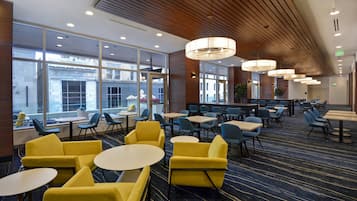 A modern hotel lobby with yellow and blue seating, large windows, and a patterned carpet.