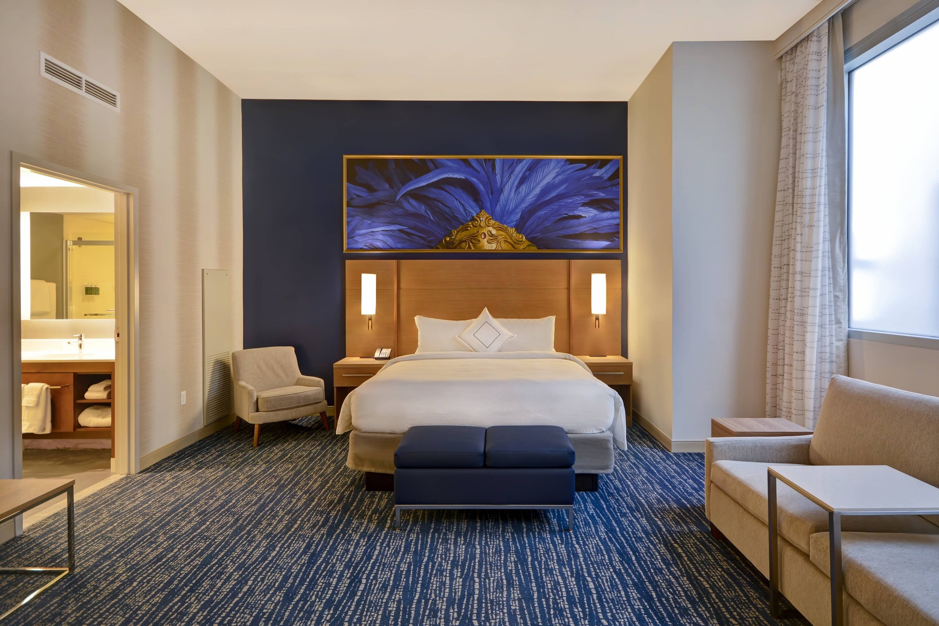 Une chambre d’hôtel avec un grand lit, deux tables de chevet, une chaise, une petite table et une grande fenêtre.