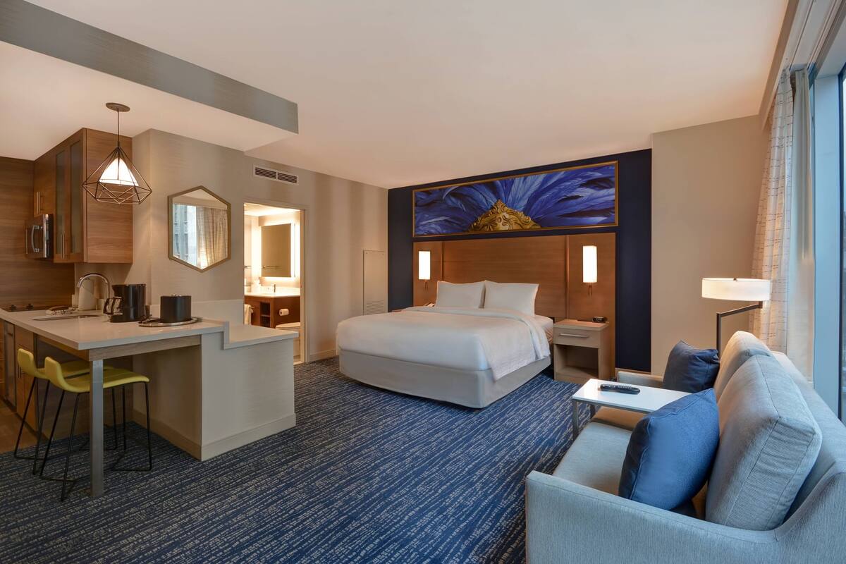 A hotel room with a bed, a desk, a chair, a sofa, and a large window.