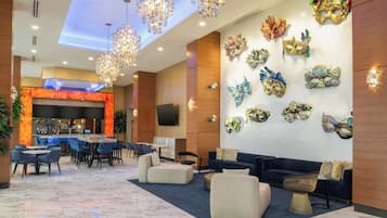Een ruime lobby met een bar, zitgedeeltes en decoratieve maskers aan de muur.