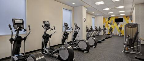 Une salle de sport équipée de plusieurs tapis de course, de vélos d’appartement et d’appareils de musculation.