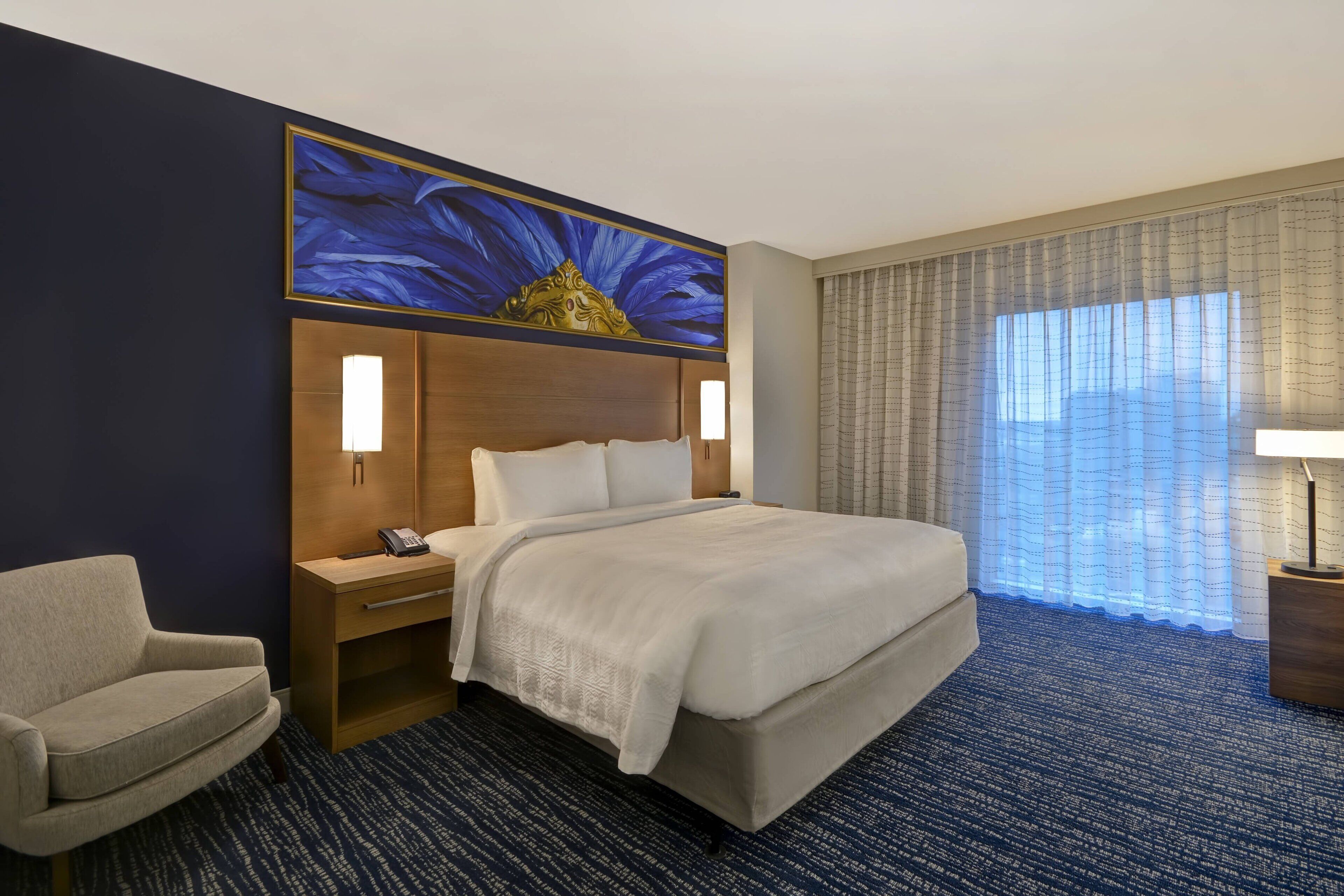 A hotel room with a large bed, a desk with a telephone, a chair, and a decorative wall piece.